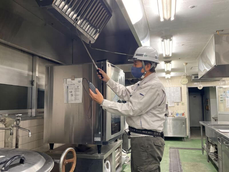 厨房の排気フードに測定器具を当てて法定検査を行うコーセイの建築設備検査員