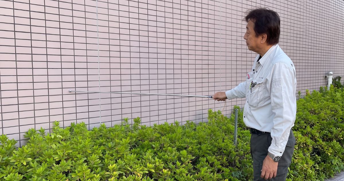 ビルの外壁を打診棒を使って慎重に調査する特定建築物調査員